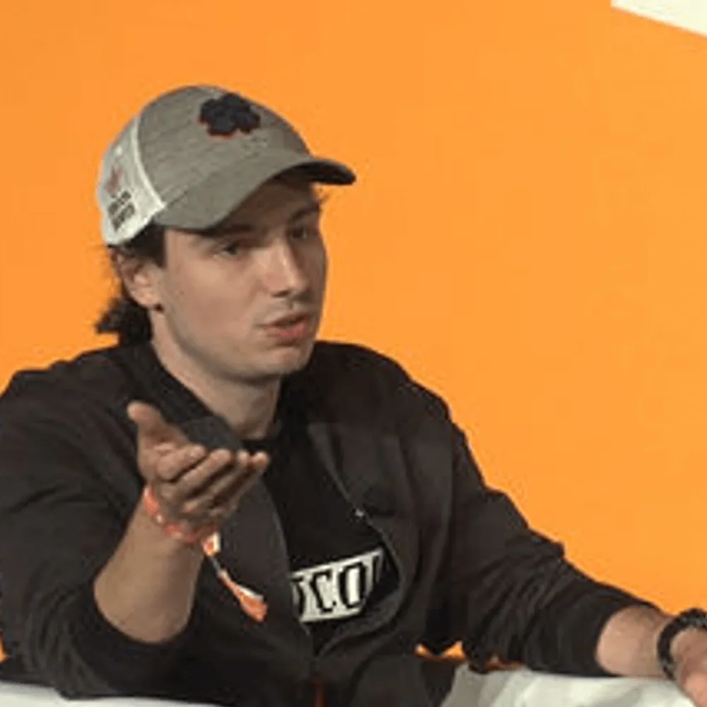 Man wearing a “Bull Bitcoin” shirt speaking on camera in a home office setup.