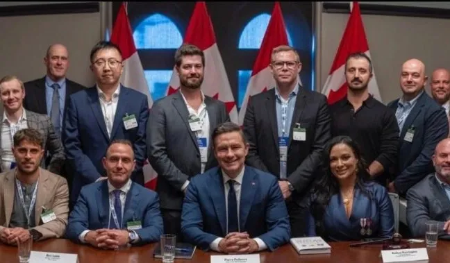Group photo of Canadian MPs and Bitcoin industry leaders at Bitcoin on the Hill 2025, with Pierre Poilievre seated center, Canadian flags in the background.